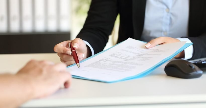 Close up of an executive hands holding a pen and indicating where to sign a contract at office